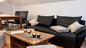 Ein modernes Wohnzimmer mit einem schwarzen Ledersofa, einem Holztisch mit Blumenvase und einem Essbereich mit Stühlen und Tisch.