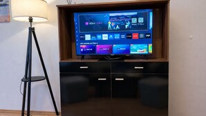 Ein Flachbildfernseher an einem Holzkasten befestigt, mit einer digitalen Benutzeroberfläche, die verschiedene Sender und Apps anzeigt.