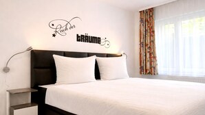 A bedroom with a bed, two pillows, a bedside table, a wall-mounted lamp, and a window with curtains. - Welcome to “Donnerkeil” – your cozy seaside hideaway. (Ostseebad Binz)