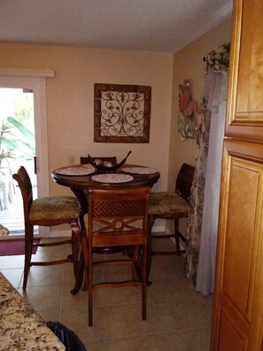 A dining area with a round table, four chairs, and a decorative wall piece. - Lovely 2-bedroom condo with heat pool in great location (Fort Myers)