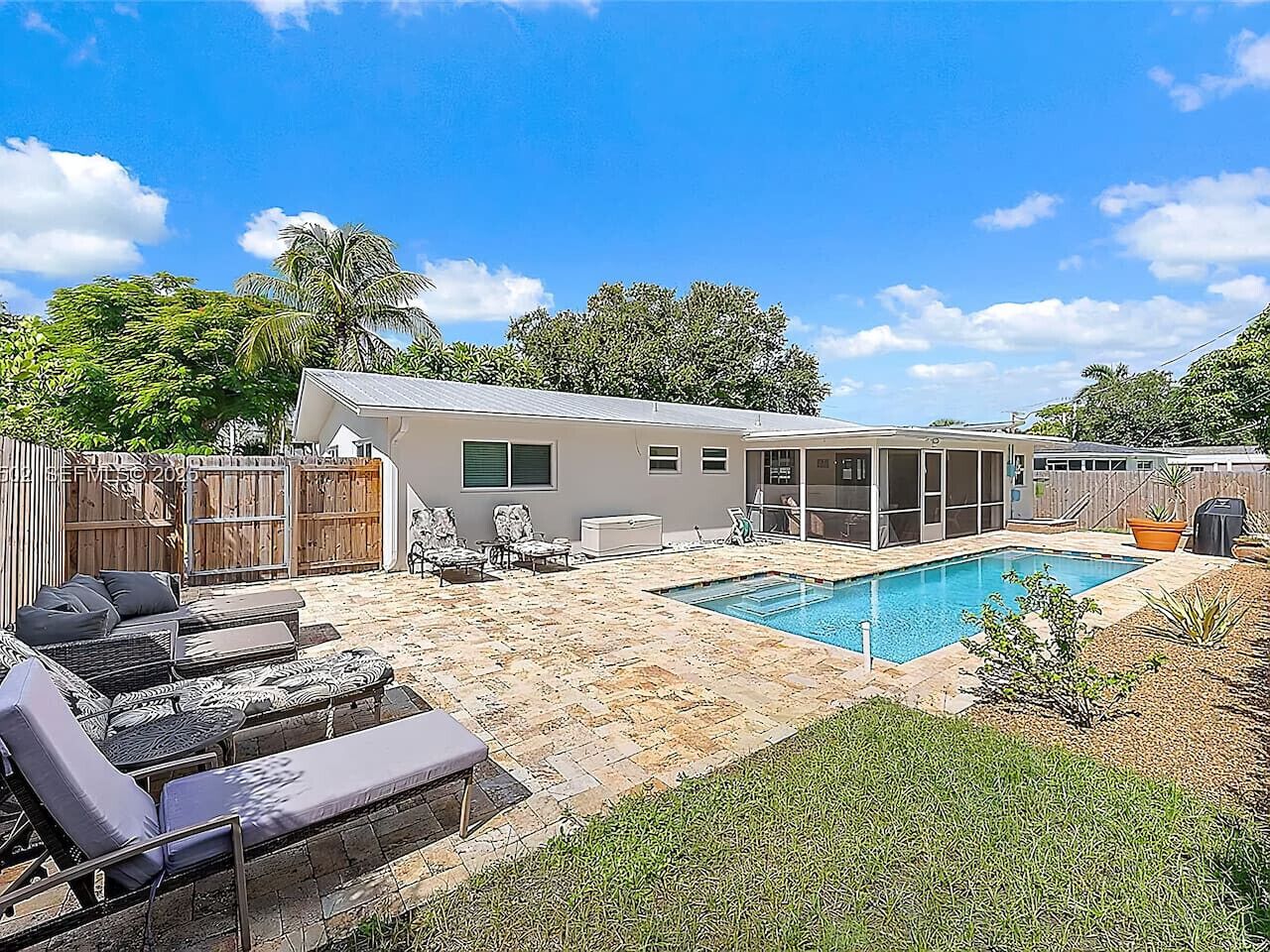 Una casa moderna con piscina, mobiliario de exterior y patio cercado.