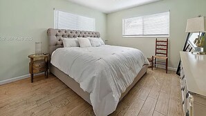 Un dormitorio con una cama grande, dos mesitas de noche, un aparador, una silla y una ventana con persianas.