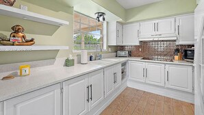 Una cocina con armarios blancos, suelo de madera y ventana con vista a zonas verdes.