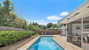 Una piscina rectangular con borde de azulejos, rodeada por una valla de madera y abundante vegetación.