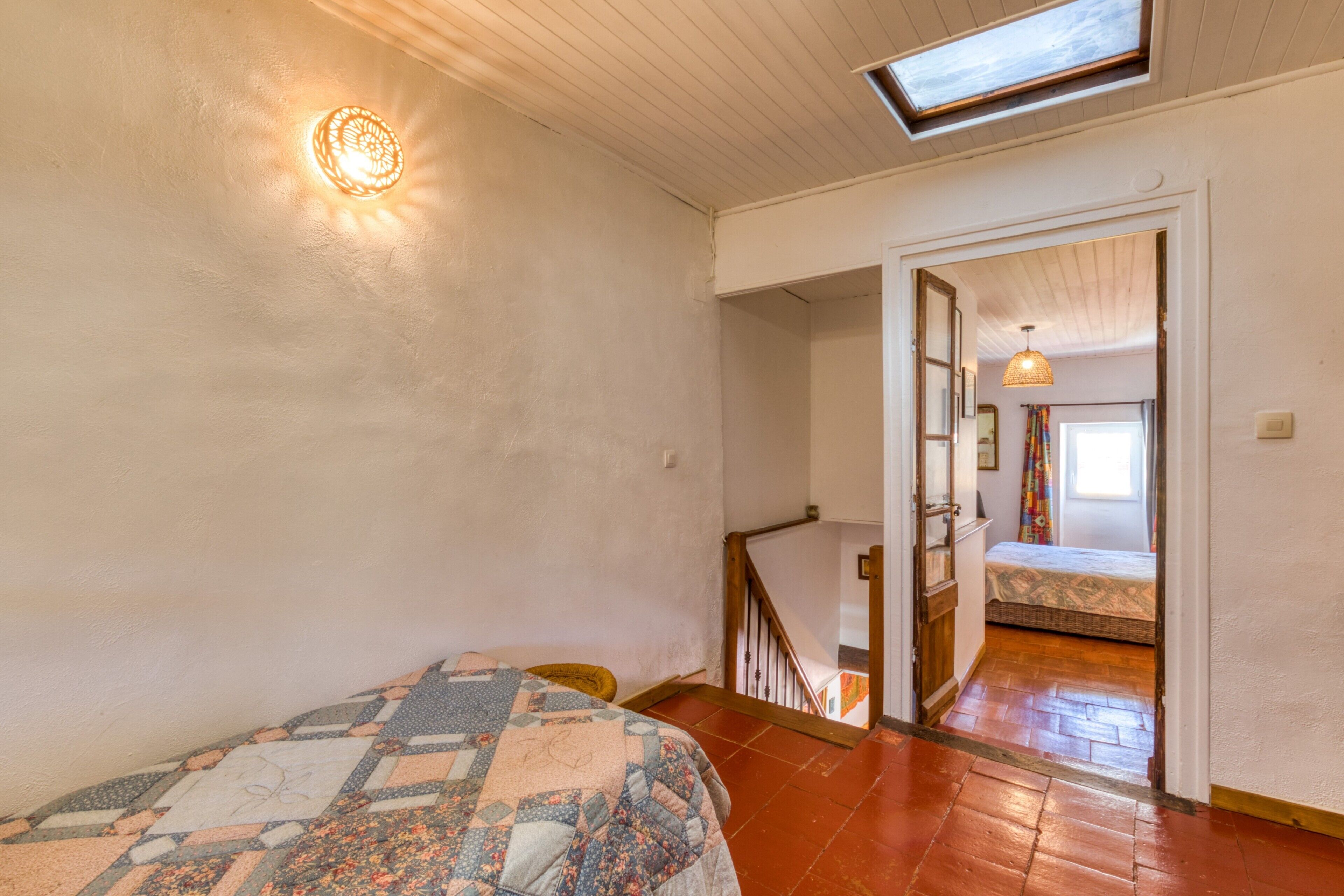 Un dormitorio con cama, tragaluz, escalera y vista a otra habitación.