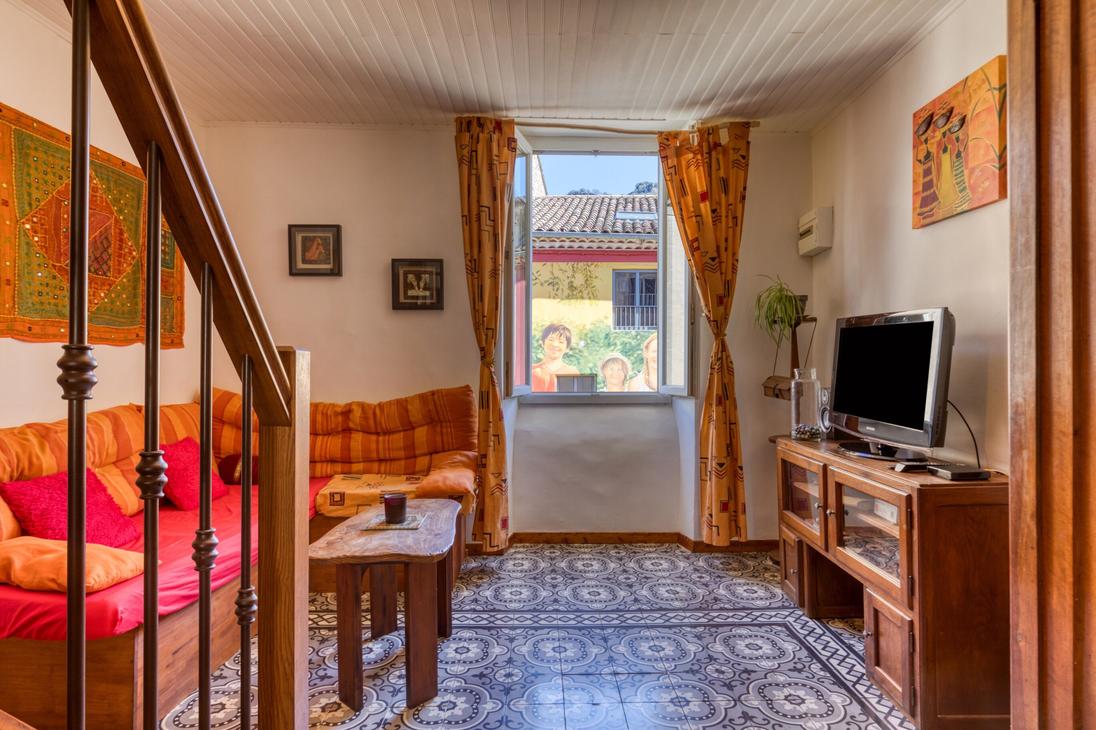 A living room with a sofa, a television, a patterned floor, and a window with curtains.
