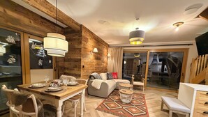 Una sala moderna con una pared de acento de madera, una zona de comedor con sillas blancas, un sofá y una alfombra estampada.