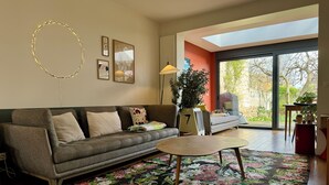 Una sala de estar con un sofá, una mesa de centro, un tapete floral y un ventanal con vistas a árboles.