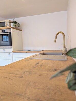 A kitchen with a wooden countertop, a stainless steel sink with a gold faucet, and a built-in oven. - Trompette - Charming accommodation at the foot of the Vosges mountains (Buhl)