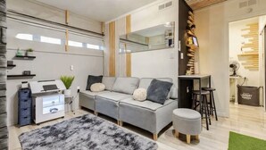 A modern living room with a grey sofa, a small round ottoman, a fluffy rug, a mirror, and a wooden shelf. - Private Cinematic Zen Loft\Spa Tub — 6PM–10AM (Orlando)
