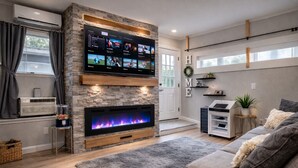 A living room with a fireplace, a flat-screen TV mounted on a stone wall, and a sofa. - Private Cinematic Zen Loft\Spa Tub — 6PM–10AM (Orlando)