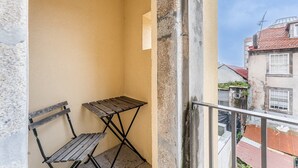 Een balkon met een houten bankje en een kleine tafel, een helder uitzicht op de aangrenzende gebouwen en een metalen hekwerk.