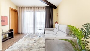 Una sala de estar moderna con un sofá gris, un banco de madera, una mesita redonda y un ventanal con cortinas traslúcidas.