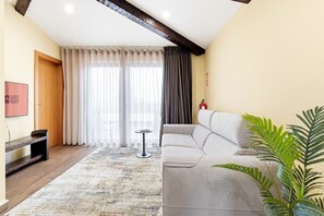 A modern living room with a grey sofa, a wooden bench, a small round table, and a large window with sheer curtains. - GuestReady - Poveiros Flats | Pique Suite/Terrace (Porto)