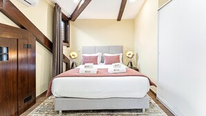 Una habitación de hotel con una cama grande, vigas de techo de madera, un cabecero, lámparas de noche y un armario.