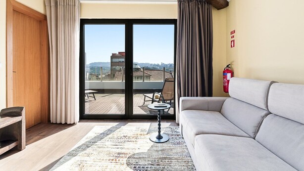 Una sala de estar moderna con un sofá, una mesita y vistas a la ciudad a través de amplios ventanales.