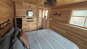 Un dormitorio de cabaña de madera con una cama, un espejo, una araña y una ventana.