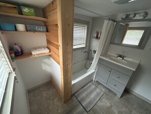 Ein Badezimmer mit Holzregal, Badewanne, Dusche und Waschtisch mit Spiegel.
