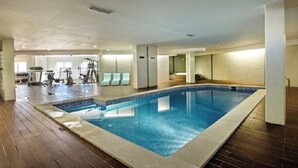 An indoor swimming pool with a wooden floor surrounding it, a fitness area with exercise equipment, and a seating area with chairs. - Excellent Private Penthouse with lots of space (Lagos)