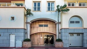 A multi-story building with a central wooden archway entrance, two palm trees, and a garage door on the right. - Excellent Private Penthouse with lots of space (Lagos)