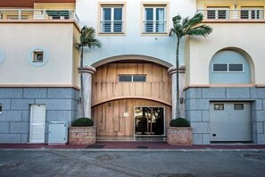 A multi-story building with a central wooden archway entrance, two palm trees, and a garage door on the right. - Excellent Private Penthouse with lots of space (Lagos)