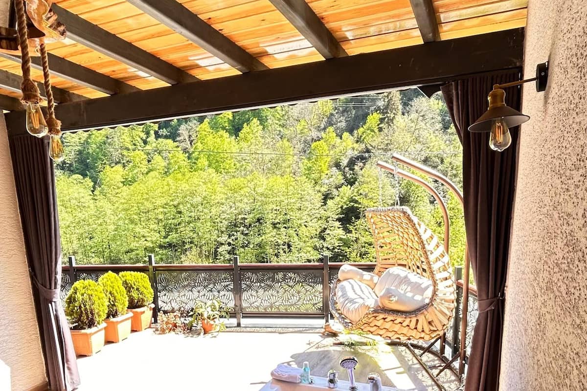 A hot tub with a wooden deck, surrounded by a wooden pergola, with a view of greenery and a decorative chair.