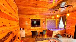 Een knus kamer in chaletstijl met houten wanden, een bed met een gestreept deken, een klein bureau en een televisie.