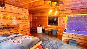 Een houten hut van binnen met een bed, een televisie, een eethoek en een open haard.