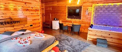A wooden cabin interior with a bed, a TV, a dining area, and a fireplace.