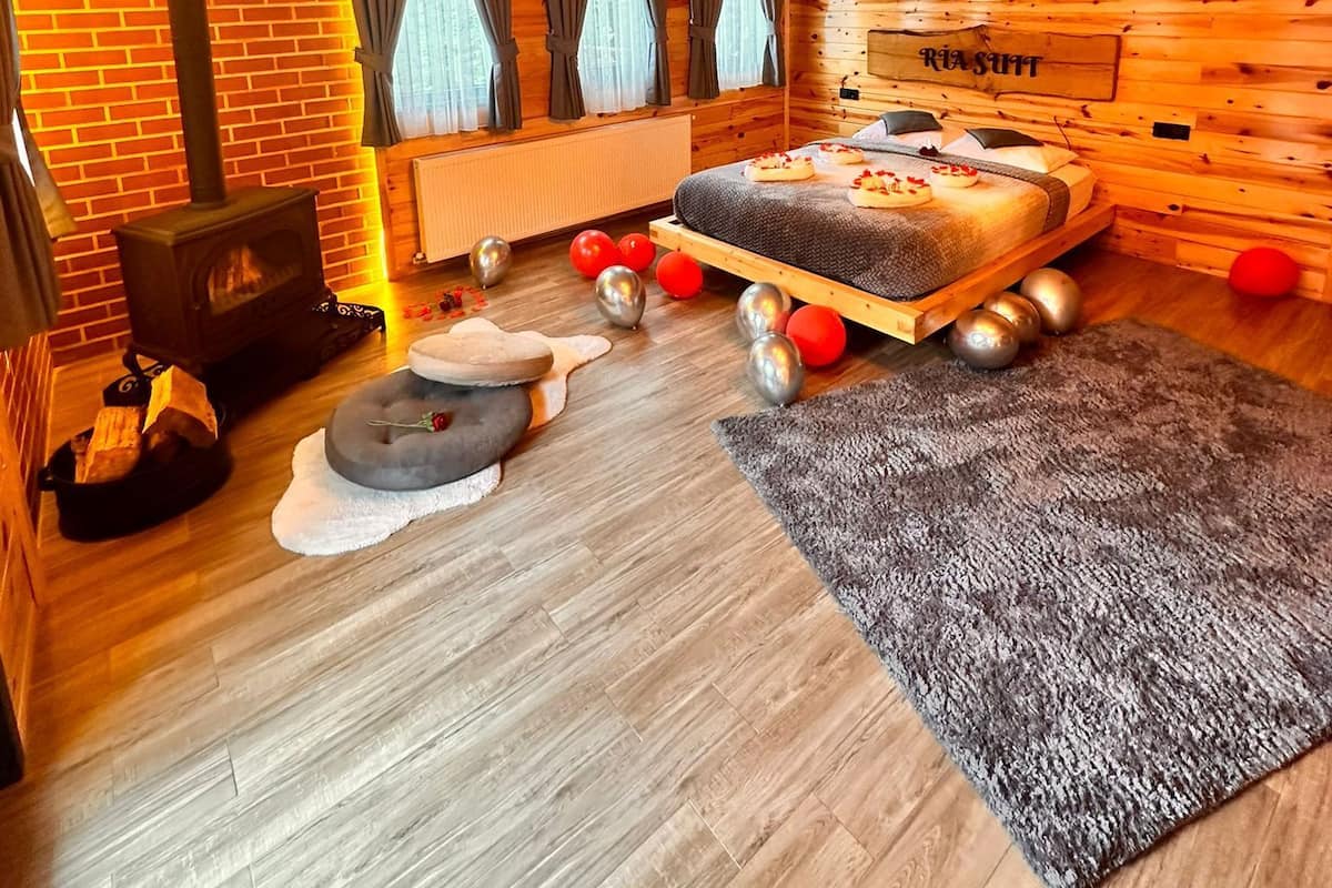A cozy log cabin room with a bed, a fireplace, and a rustic wooden ceiling.