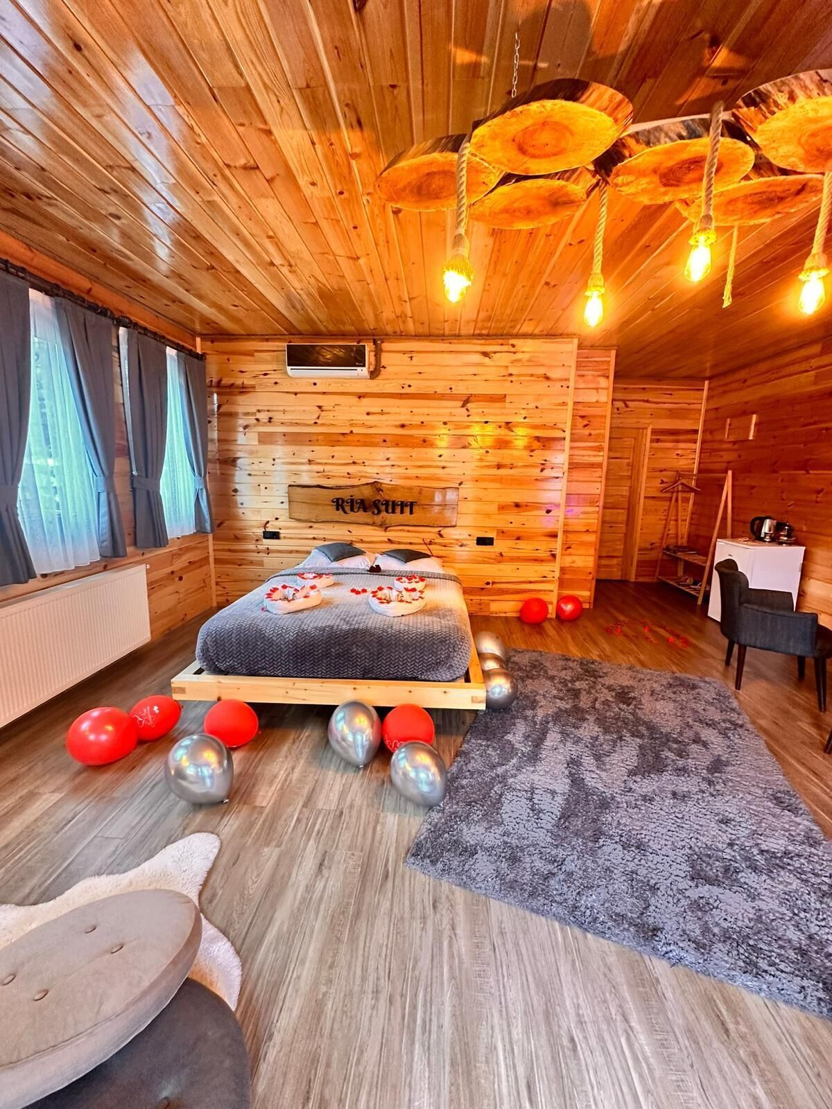 Interior de una cabaña de madera con una cama, un escritorio y una lámpara colgante.