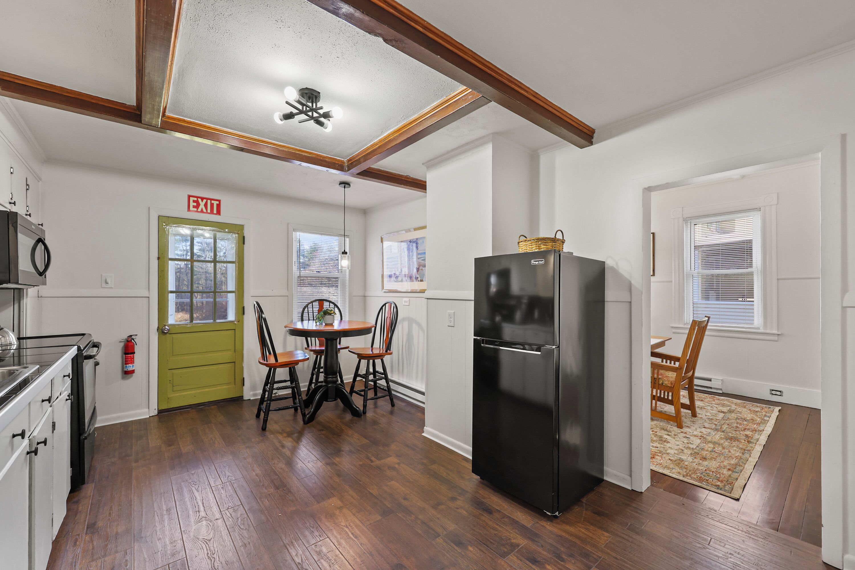 A kitchen with a black refrigerator, wooden cabinets, a dining table with chairs, and a green door marked "EXIT".