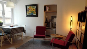 A living room with a dining table, two red chairs, a grey rug, a bookshelf, and a floor lamp. - 30-square-meter air-conditioned studio in the heart of Obernai—quiet and comfortable, with a fully equipped kitchen (Obernai)