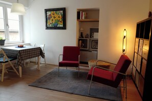 A living room with a dining table, two red chairs, a grey rug, a bookshelf, and a floor lamp. - In the heart of Obernai studio 30m2 quiet comfortable kitchen equipped air conditioning (Obernai)