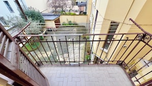 A balcony with a metal railing, a tiled floor, and a view of a courtyard with plants and a building in the background. - B91 by VIDI · Bright Milanese flat near Navigli, direct tram to Duomo (Milano)