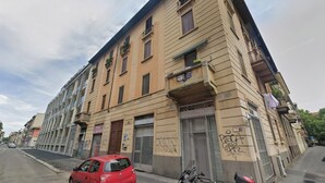 A multi-story building with a closed shop on the ground floor, a parked red car, and a scooter on the sidewalk. - B91 by VIDI · Bright Milanese flat near Navigli, direct tram to Duomo (Milano)