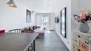 A modern living room with a dining area, a sofa, a TV, and a decorative vase. - LA PLAGE Roses / Roses - INTERimmo (Rosas / Roses)