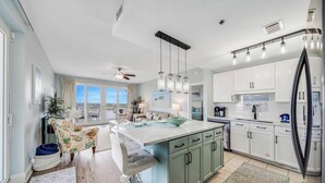 Cocina moderna con una isla grande, armarios blancos y vistas al exterior.