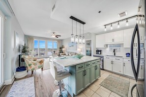 A modern kitchen with a large island, white cabinets, and a view to the outside. - Coral Corner Getaway (Panama City Beach)