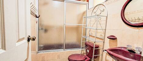 A bathroom with a toilet, sink, shower, and a metal shelf.