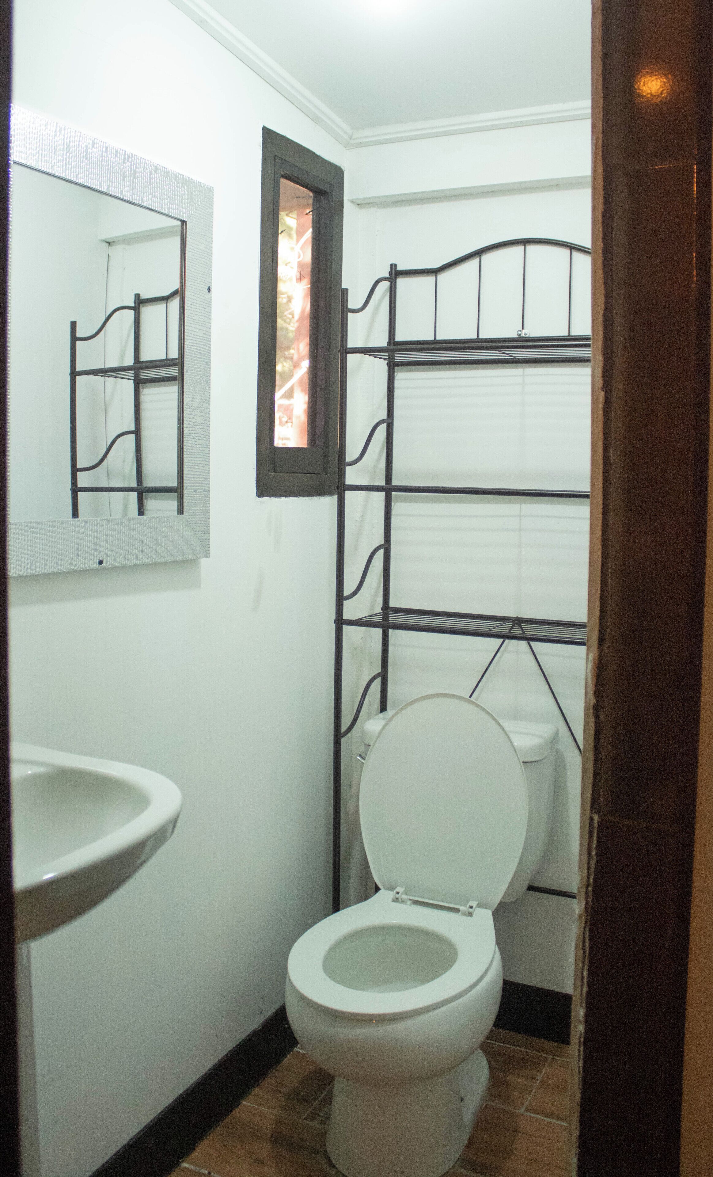 Un baño con inodoro, lavamanos y una estantería metálica.