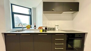 Cozinha moderna com forno embutido, uma janela grande e bancada com diversos utensílios de cozinha.