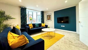 Uma sala de estar moderna com sofá, mesa de centro e TV fixada em uma parede azul-turquesa.