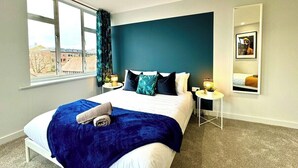 Quarto de hotel moderno com uma cama grande, vista da cidade e mesa de cabeceira com abajur.