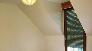 A bedroom with a sloped ceiling, a bed with a patterned bedspread, a green blanket, and a window with blinds. - Charming house 40 min from Paris (Bondoufle)