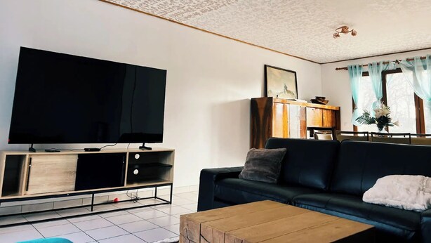 A living room with a flat-screen TV, a dark-colored sofa, a wooden coffee table, and a cabinet with drawers. - Charming house 40 min from Paris (Bondoufle)