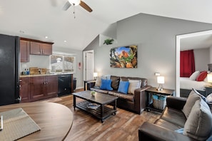 A modern living room with a brown leather sofa, a wooden coffee table, and a kitchen area with dark cabinets and a dishwasher.
