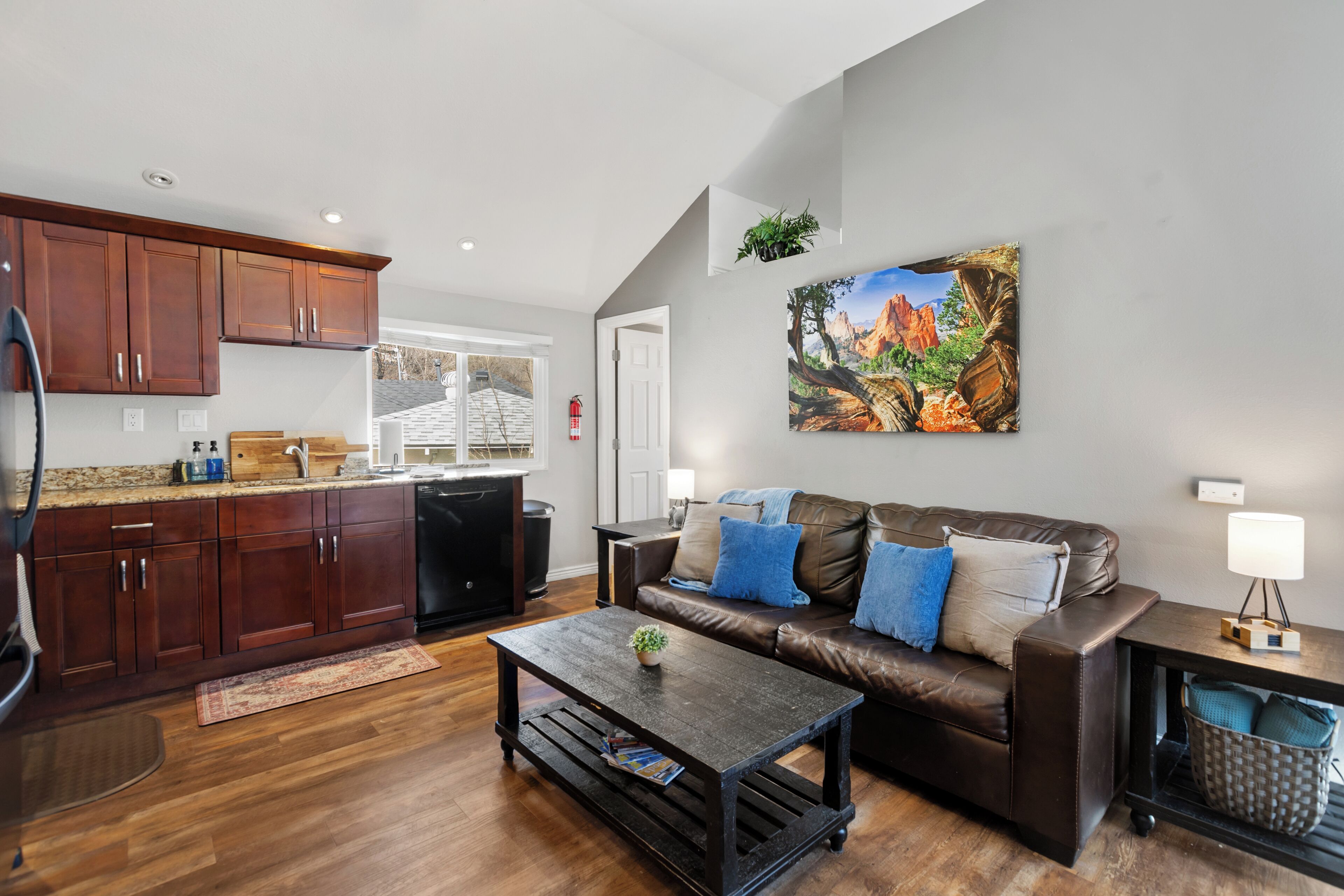 A modern living room with a brown leather sofa, a coffee table, and a painting of a mountain landscape.