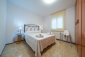 A bedroom with a bed, bedside lamps, a radiator, a window with blinds, and a chair. - HomeHolidaysRentals Magic - Costa Barcelona (Pineda de Mar)