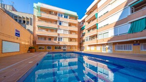 En swimmingpool omgiven av flerfamiljshus med balkonger och ett område med kakelplattor runt poolen.